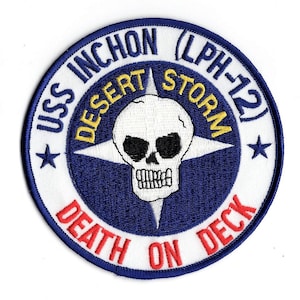 Puede incluir: Un parche bordado blanco con un círculo azul que contiene una calavera blanca con ojos negros y una estrella amarilla. El texto alrededor del círculo dice "USS INCHON (LPH-12) DESERT STORM DEATH ON DECK".