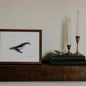Peut inclure: Une illustration en noir et blanc encadr&eacute;e d'une baleine &agrave; bosse, avec un cadre en bois et un passe-partout blanc. L'illustration est sur une &eacute;tag&egrave;re avec deux chandeliers et un petit bol.