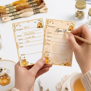 Puede incluir: Dos tarjetas rectangulares de seguimiento de proyectos con temática de abejas y miel, que incluyen campos para Designer, Chart, Fabric, Floss, Date y Notes. Las tarjetas están decoradas con ilustraciones de colmenas, tarros de miel y flores.