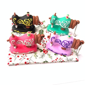 Peut inclure: Quatre porte-clés miniatures en forme de machine à coudre de différentes couleurs : noir, vert, rose et violet. Chaque porte-clés est orné d’un motif floral décoratif et d’une petite chaîne.
