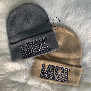 Puede incluir: Dos gorros de punto con la palabra "MAMA" en estampado de cuadros blanco y negro. Un gorro es gris y el otro beige.
