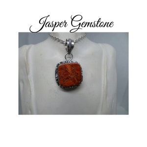 May include: A silver chain necklace with a square pendant featuring a red jasper gemstone. The pendant has a detailed silver frame.
