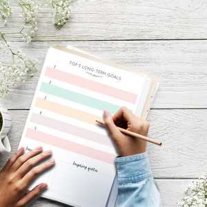 May include: A printable worksheet with the title "Top 5 Long-Term Goals" with five lines for writing goals. The worksheet is on a white wooden table with a cup of green tea and white flowers.