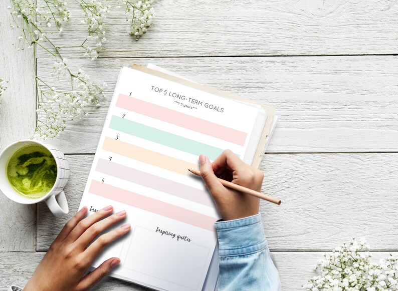 May include: A printable worksheet with the title "Top 5 Long-Term Goals" with five lines for writing goals. The worksheet is on a white wooden table with a cup of green tea and white flowers.