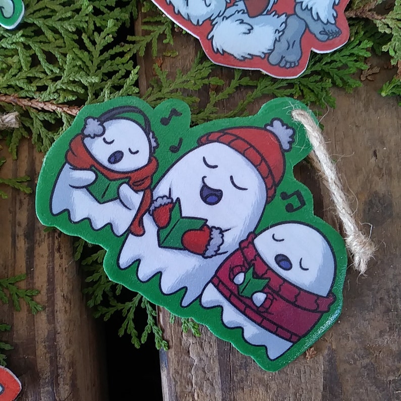 May include: Three white ghosts wearing winter clothing and singing Christmas carols. The ghosts are wearing red and green scarves, hats, and mittens. The ghosts are on a green background with musical notes.