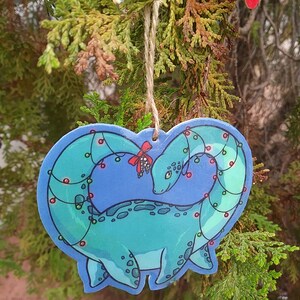 K&ouml;nnte beinhalten: Ein blauer und gr&uuml;ner Weihnachtsbaumschmuck in Form eines Dinosauriers mit einer Lichterkette drumherum.