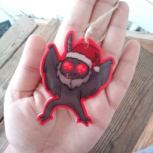 K&ouml;nnte beinhalten: Ein roter und grauer Weihnachtsbaumschmuck in Form eines Cartoon-Monsters, das eine Weihnachtsm&uuml;tze tr&auml;gt. Das Monster hat gro&szlig;e rote Augen und einen wei&szlig;en Bart.