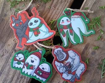 Könnte beinhalten: Fünf Weihnachtsornamente mit verschiedenen Figuren. Die Ornamente sind aus Papier und haben ein rot-grün-weißes Farbschema. Die Figuren umfassen einen Yeti, der eine Tasse hält, ein Gespenst, das Weihnachtslieder singt, eine Motte mit einem roten Schal, einen Schneemann mit einem roten Schal und zwei Gespenster, die sich an den Händen halten.