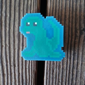 May include: A blue pixelated frog sitting on a wooden surface. The frog has large eyes and a small mouth.