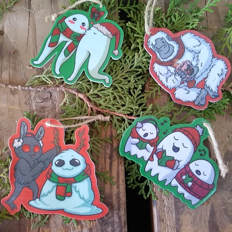 May include: Four Christmas ornaments featuring cartoon characters. A yeti holding a mug, a bat and a snowman, and two ghosts singing Christmas carols.