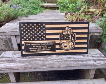 May include: Wooden plaque featuring a carved American flag design with stars and stripes. Includes the USN emblem and text: "Chief Petty Officer Frank Schweitzer, 23 Years of service, September 1972 - March 1995, At ease, we have the watch."