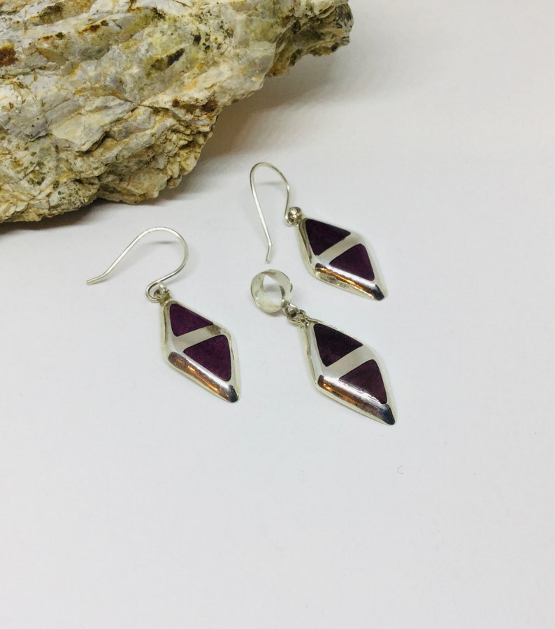 May include: A set of silver earrings and a pendant with purple and white diamond-shaped stones.