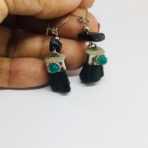 May include: A pair of dangle earrings with black tassel-like charms, silver accents, and green gemstone accents.