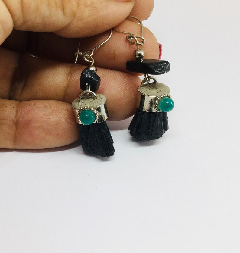 May include: A pair of dangle earrings with black tassel-like charms, silver accents, and green gemstone accents.