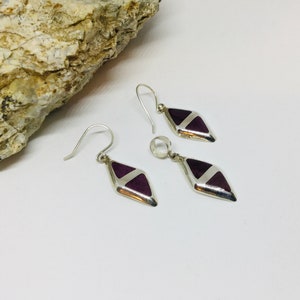 May include: A set of silver earrings with purple and white geometric designs. The earrings are shaped like diamonds and have a dangling design.
