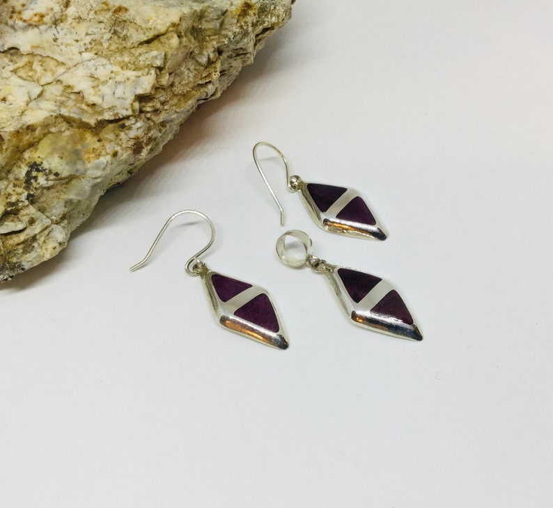 May include: A set of silver earrings with purple and white geometric designs. The earrings are shaped like diamonds and have a dangling design.
