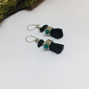 May include: A pair of dangle earrings with black tassel charms and green gemstone accents. The earrings have silver-toned metal findings.