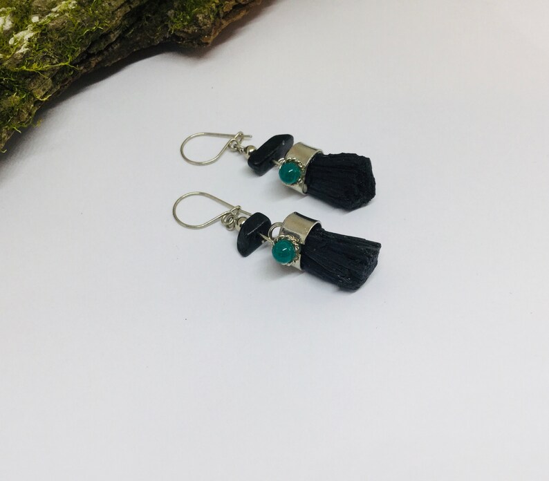 May include: A pair of dangle earrings with black tassel charms and green gemstone accents. The earrings have silver-toned metal findings.