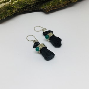 May include: A pair of earrings featuring black tourmaline stones and green gemstone accents. The earrings are made with silver wire and have a simple, elegant design.