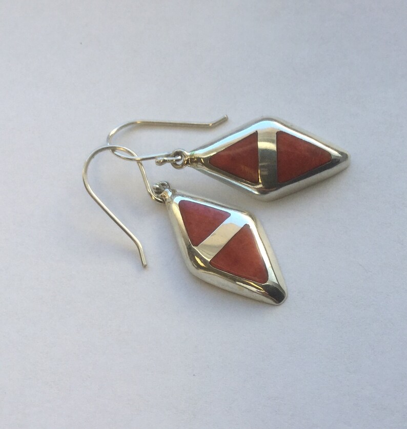 May include: A pair of silver earrings with a diamond-shaped red stone set in each earring.