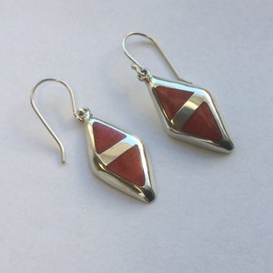 May include: A pair of silver earrings with a diamond-shaped red stone inlay.