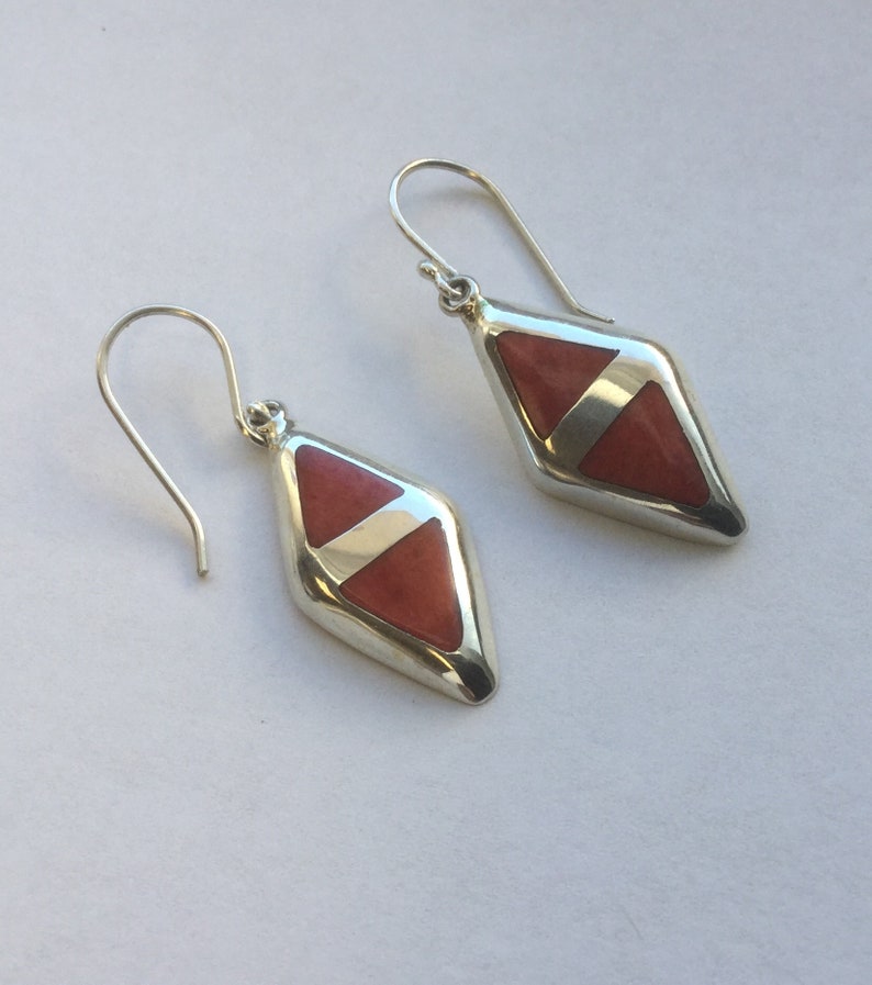 May include: A pair of silver earrings with a diamond-shaped red stone inlay.
