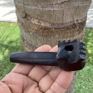 May include: A black wooden smoking pipe with a carved design. The pipe is held in a hand.