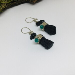 May include: A pair of silver earrings with black and green stones. The earrings are made of silver and have a black stone with a green stone on top. The earrings are hanging from a silver hook.