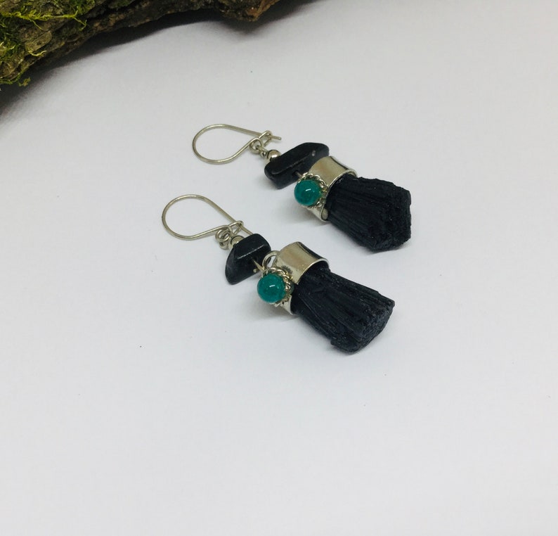 May include: A pair of silver earrings with black and green stones. The earrings are made of silver and have a black stone with a green stone on top. The earrings are hanging from a silver hook.