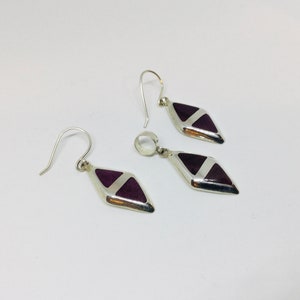 May include: A set of silver earrings and a pendant featuring a purple and white geometric design.