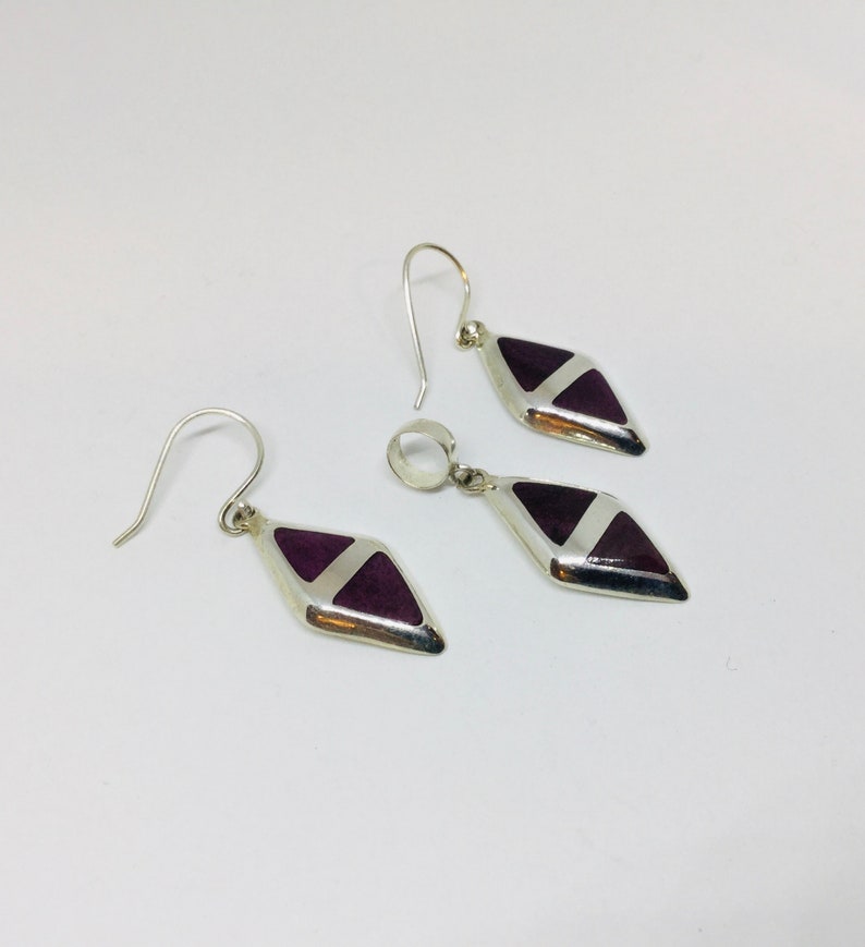 May include: A set of silver earrings and a pendant featuring a purple and white geometric design.