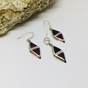 May include: A set of silver earrings and a pendant with purple diamond-shaped stones.