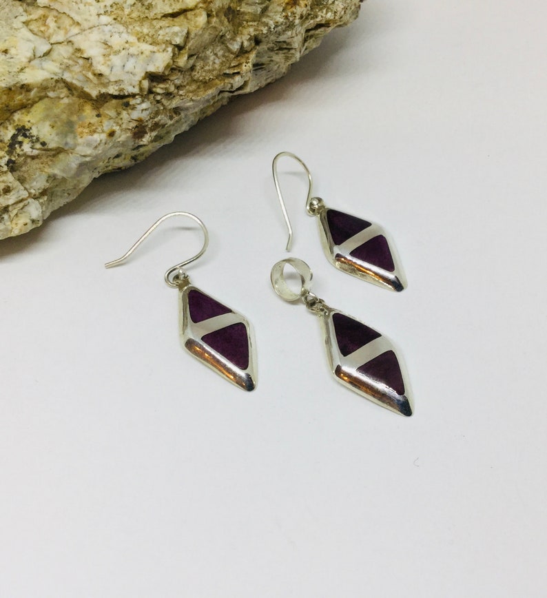 May include: A set of silver earrings and a pendant with purple diamond-shaped stones.
