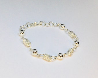 Puede incluir: Un brazalete de plata con un diseño de cadena y pequeñas cuentas redondas. El brazalete tiene un diseño de alambre retorcido entre algunas de las cuentas.