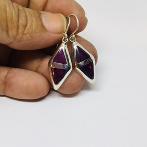 May include: A pair of silver dangle earrings with a purple and white geometric design.