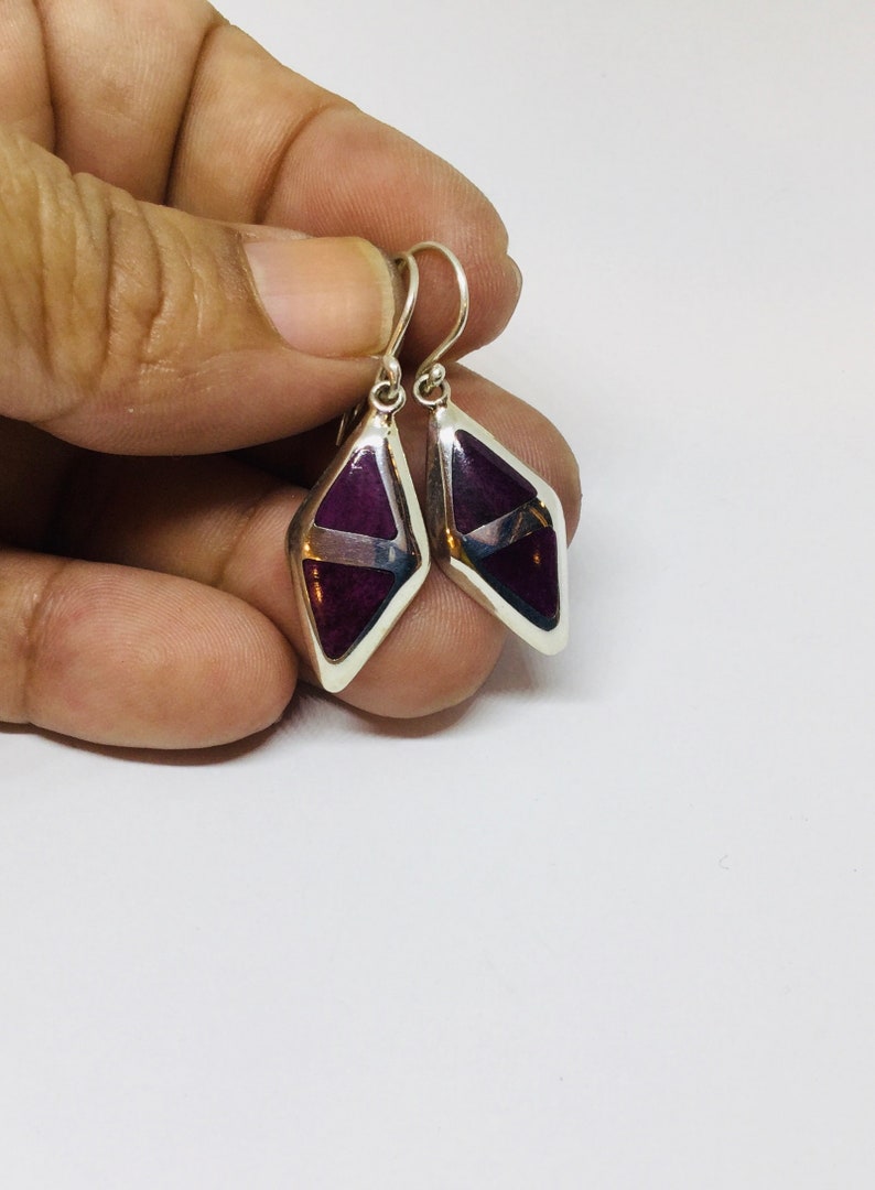 May include: A pair of silver dangle earrings with a purple and white geometric design.