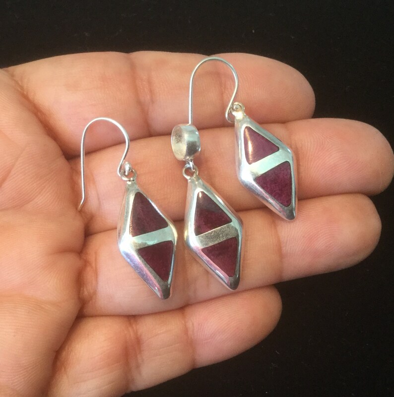May include: A set of silver earrings and a pendant featuring a geometric diamond shape with a purple stone inlay.