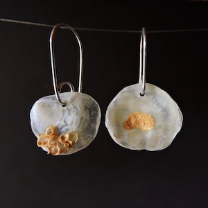 May include: A pair of drop earrings featuring irregular, translucent white shell-like discs suspended from silver-toned metal hooks. One disc displays a textured, gold-colored cluster at the base, while the other features a smooth, gold-colored patch.