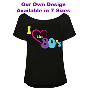 K&ouml;nnte beinhalten: Schwarzes Off-Shoulder-T-Shirt mit dem Text "I love the 80's" in Gelb, Rosa, Lila und Blau. Der Text "Our Own Design Available in 7 Sizes" steht in Lila &uuml;ber der Grafik.