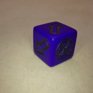 Puede incluir: Un dado morado con marcas negras. El dado tiene dos flechas apuntando en direcciones opuestas y un s&iacute;mbolo que parece una cruz con un c&iacute;rculo alrededor.