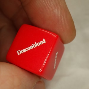 May include: A red dice with the word "Dragonblood" printed on it in white.