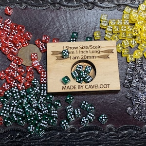 May include: A wooden sign with the text "I Show Size/Scale I am 1 Inch Long I am 20mm MADE BY CAVELOOT" surrounded by a variety of dice in different colors, including red, green, yellow, and clear.