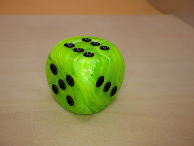 May include: A green and black dice with swirling green and white marbling. The dice has black dots on each side.