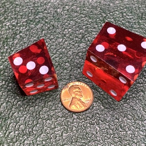 May include: Two red, clear dice with white dots. The dice are on a green surface with a 1969 penny in the middle.
