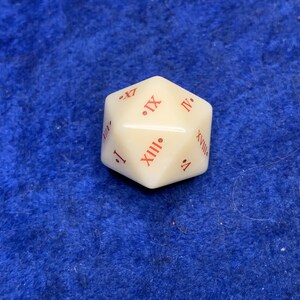 May include: Ivory-colored, multi-sided die with red Roman numerals. The die is a dodecahedron, a 12-sided shape. The numbers are clearly printed on each face, making it suitable for tabletop games.