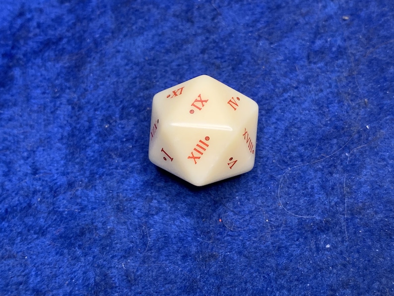 May include: Ivory-colored, multi-sided die with red Roman numerals. The die is a dodecahedron, a 12-sided shape. The numbers are clearly printed on each face, making it suitable for tabletop games.