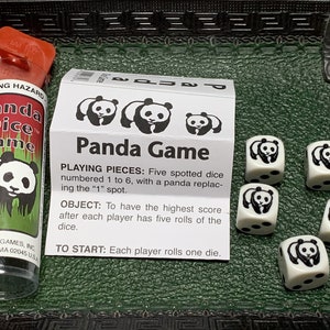 May include: A panda dice game with five white dice featuring black panda illustrations. The dice are numbered 1 to 6, with a panda replacing the "1" spot. The game instructions are printed on a white card with black text. The text reads "Panda Game", "Playing Pieces: Five spotted dice numbered 1 to 6, with a panda replacing the "1" spot.", "Object: To have the highest score after each player has five rolls of the dice.", and "To Start: Each player rolls one die."