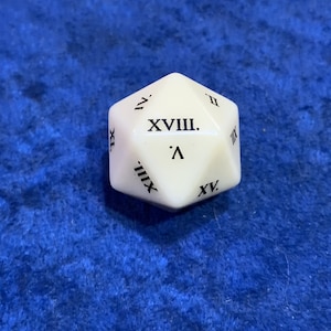 May include: A white, twenty-sided die with black Roman numerals. The die is resting on a blue surface. The die is a gaming accessory, likely for tabletop games or role-playing games.