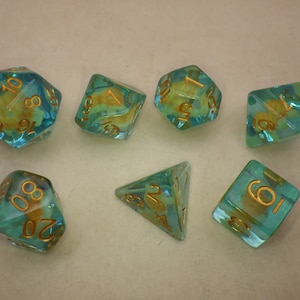 May include: Set of seven teal and gold dice with a variety of shapes and numbers. The dice are translucent and have a swirling effect.