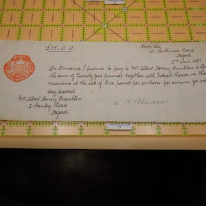 May include: An antique document with handwritten text and a red seal. The text includes the amount "£25.0.0" and the date "2nd April 1901". The document is on a yellowed paper, placed on a grid.